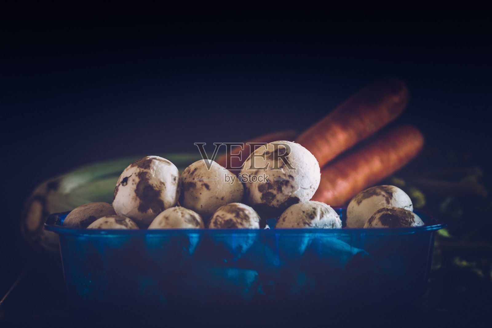 在黑色背景下的塑料容器中的新鲜生蘑菇和胡萝卜特写照片摄影图片