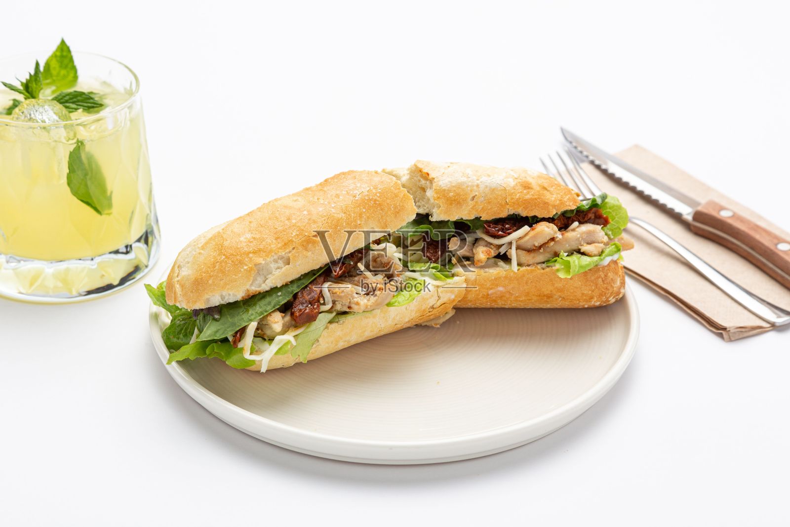 夹肉、奶酪和生菜的三明治，放在白色的陶瓷盘子里，配柠檬水和餐具照片摄影图片