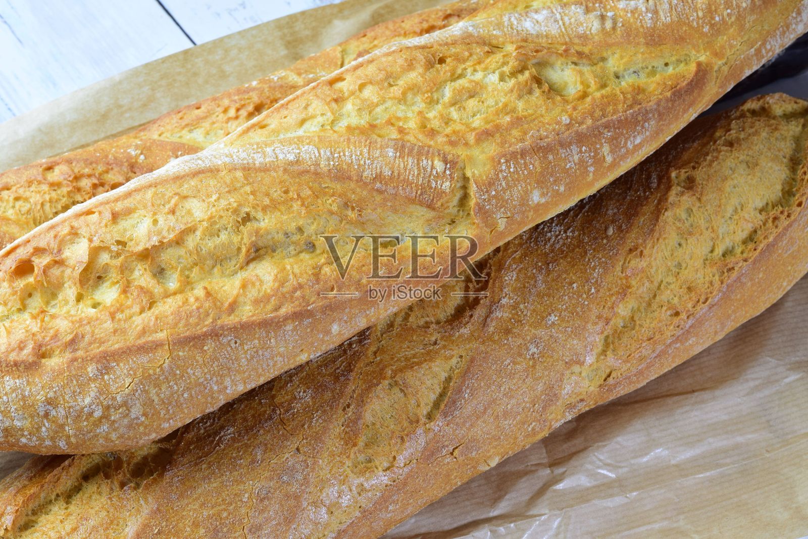 近距离拍摄新鲜出炉的牛皮纸法棍面包放在白色的桌子上照片摄影图片