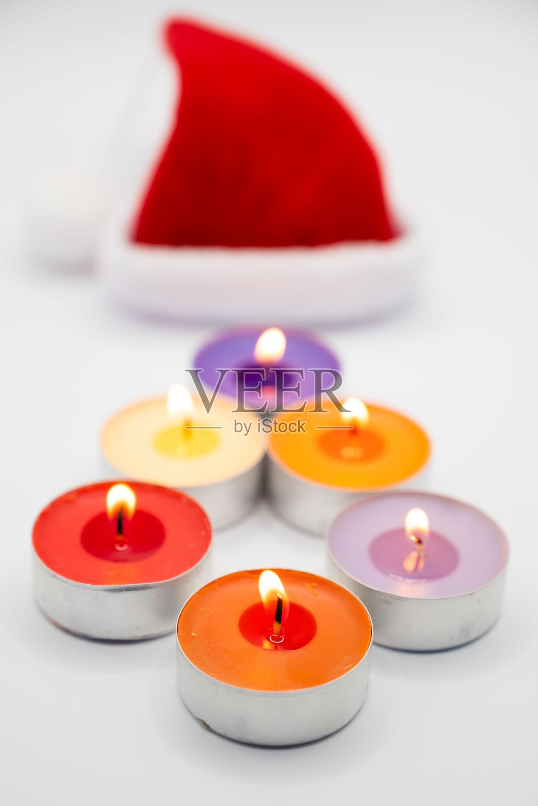 垂直拍摄彩色燃烧的蜡烛，背景是圣诞老人的帽子照片摄影图片