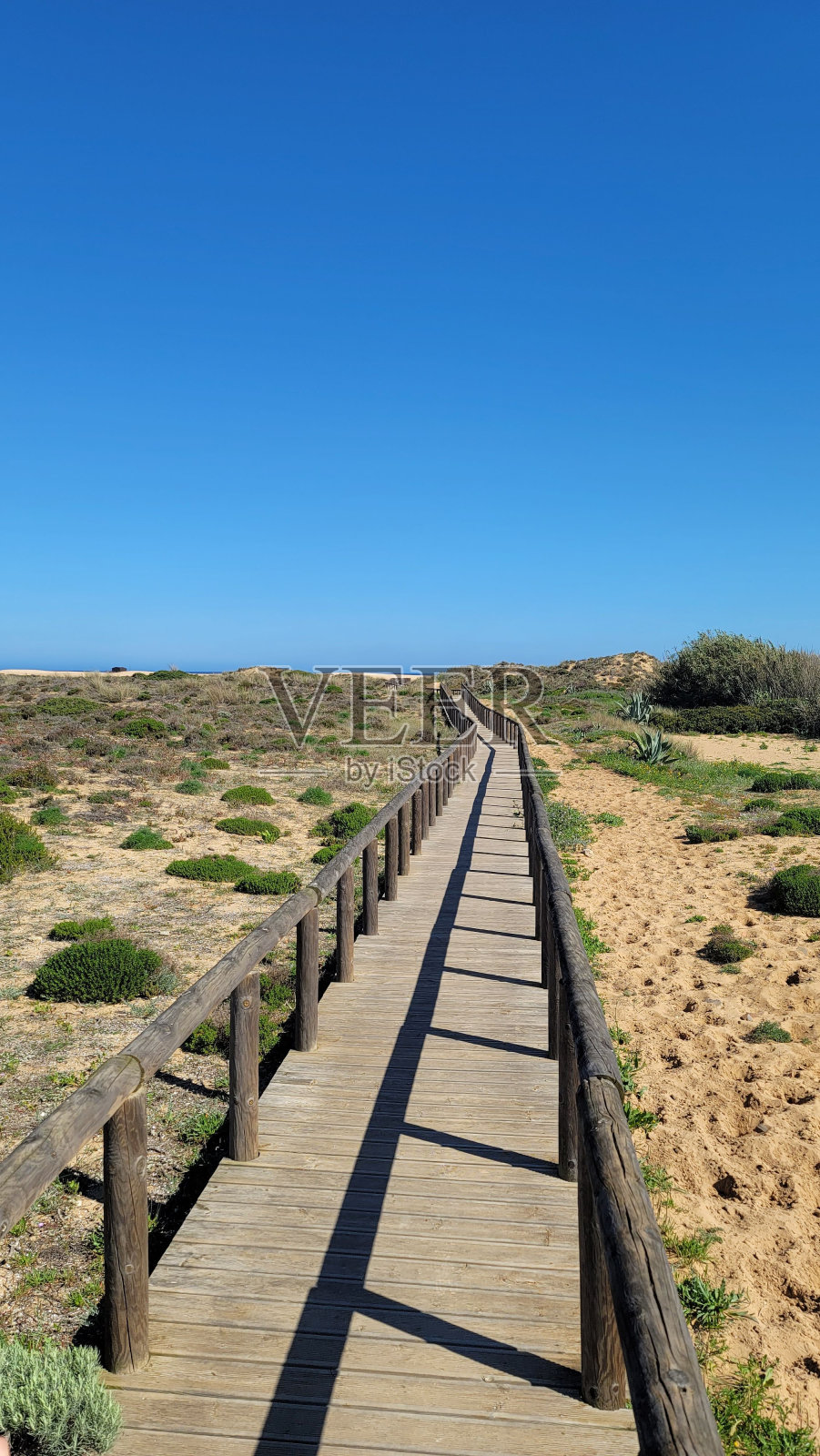 沙漠中一条木路的垂直镜头，蓝天下栏杆的倒影照片摄影图片