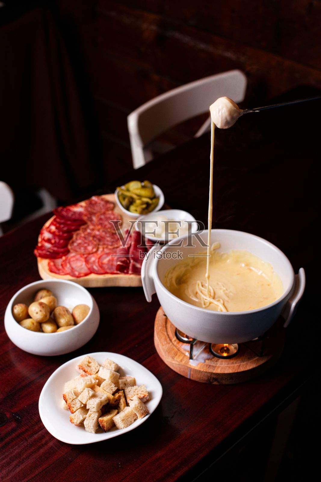 碗里放着融化的奶酪，板上放着切片香肠和咸菜，桌子上放着几片干面包照片摄影图片