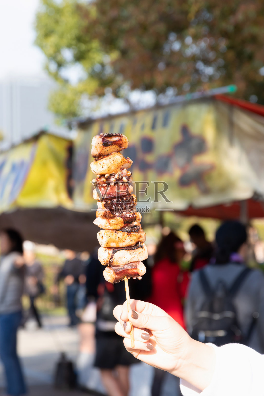 女人手拿烤章鱼串，准备吃。日本传统的大排档。照片摄影图片