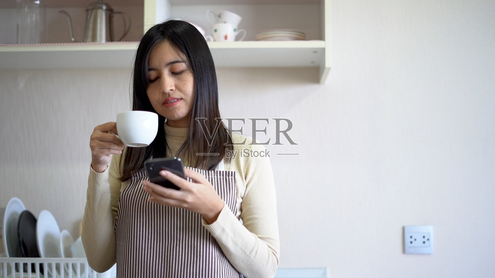 女人在厨房里用智能手机喝咖啡。照片摄影图片