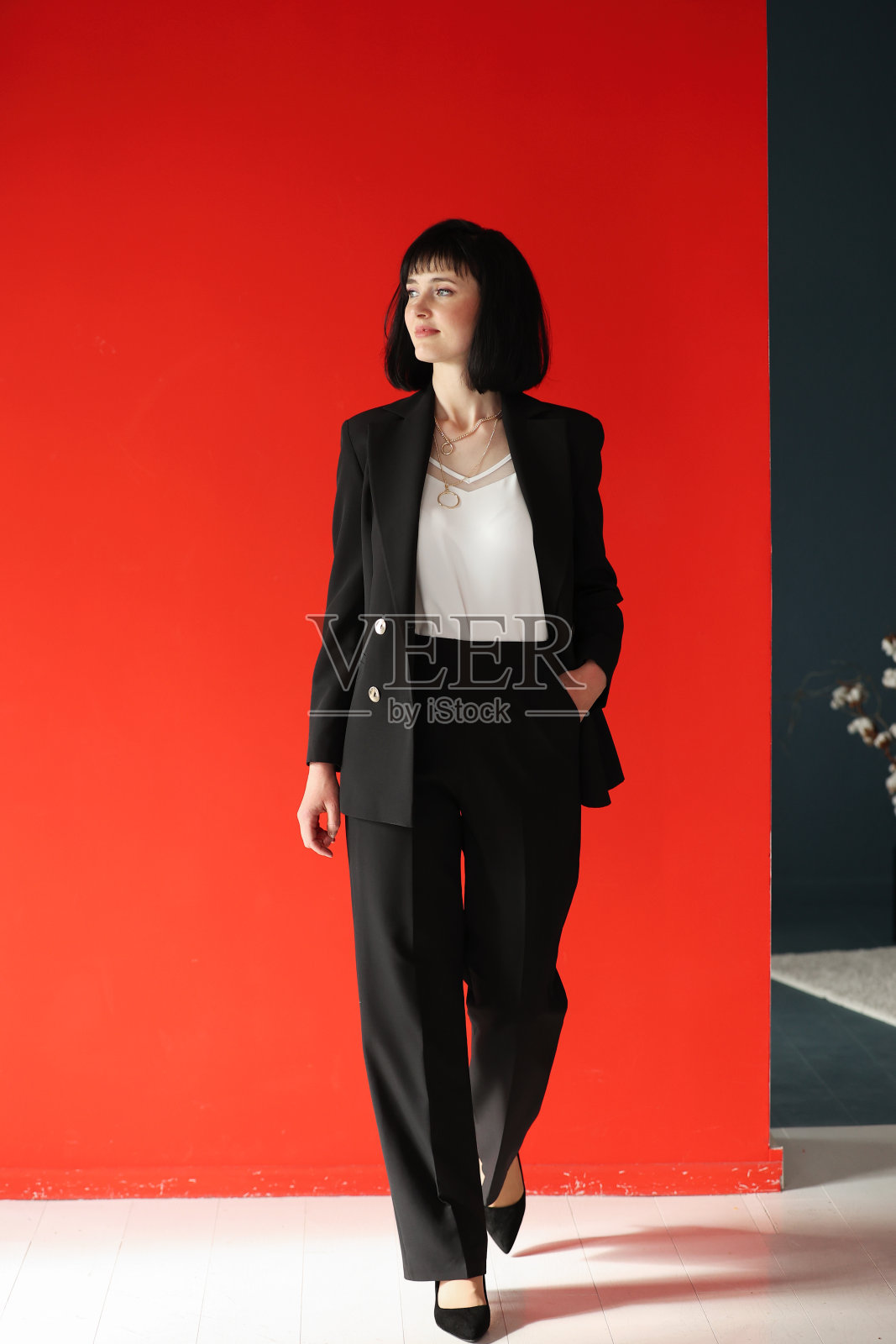 美丽的女性黑发商务女CEO在黑色西装，孤立的红色背景，自信地站在口袋里的手臂。商界女性。照片摄影图片