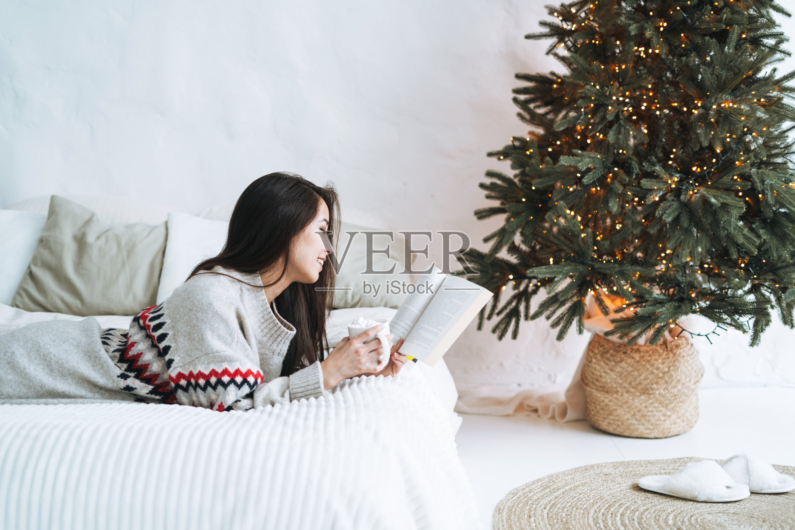 年轻的亚洲女人在家里圣诞树附近的床上看书照片摄影图片