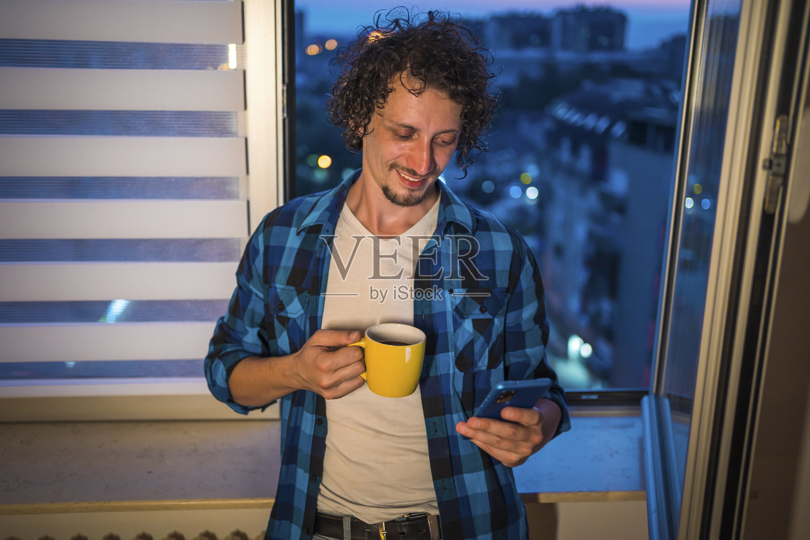 一个男人站在家里的窗户边用智能手机照片摄影图片