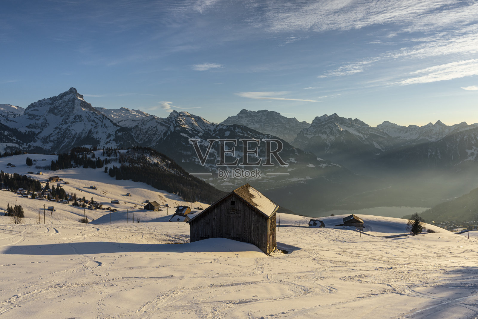 日落时分，瑞士圣加伦州，格拉鲁斯阿尔卑斯山全景前，白雪覆盖的草地和干草小屋照片摄影图片