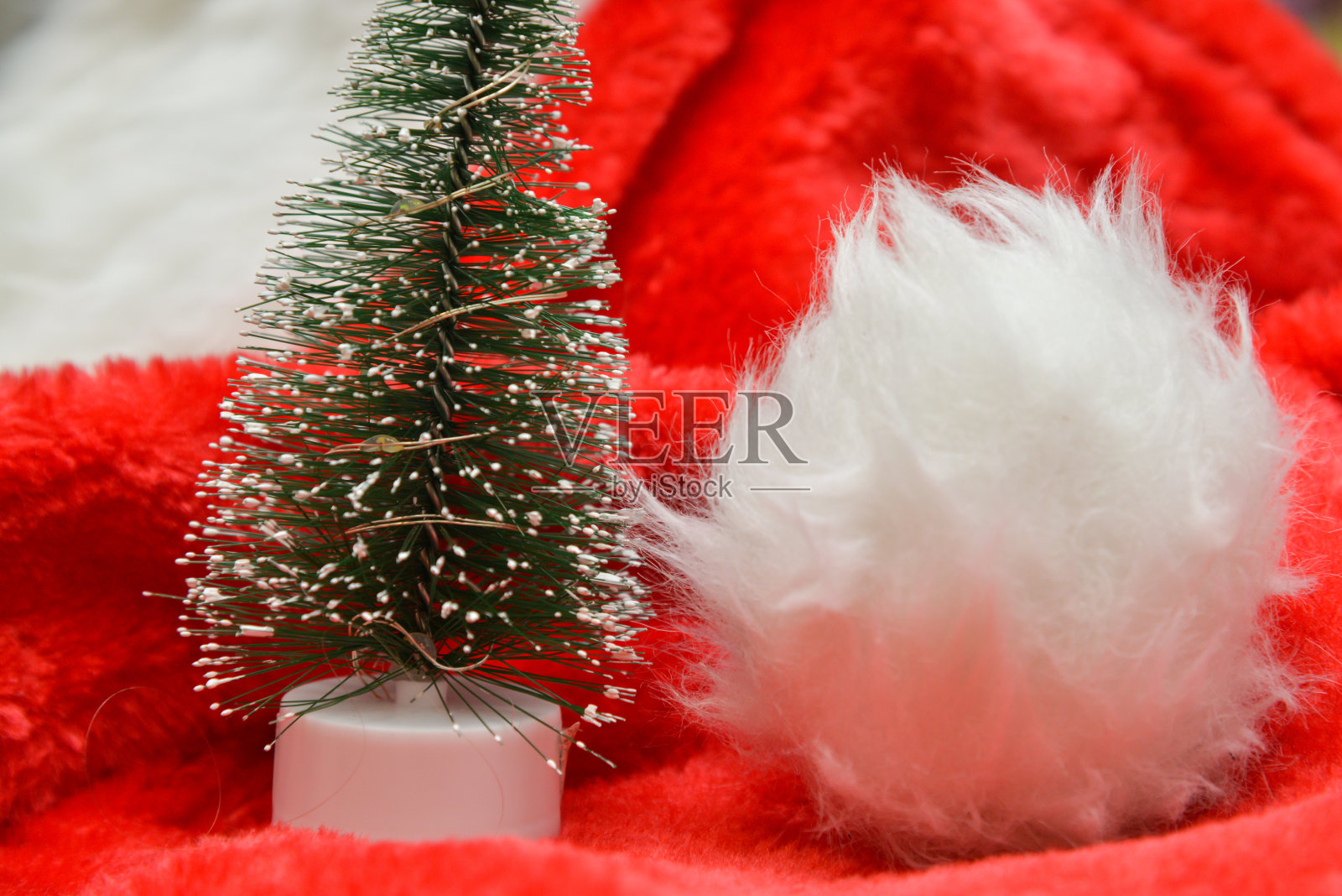 圣诞装饰品。一棵小人造圣诞树，红色圣诞老人帽上有人造雪。照片摄影图片