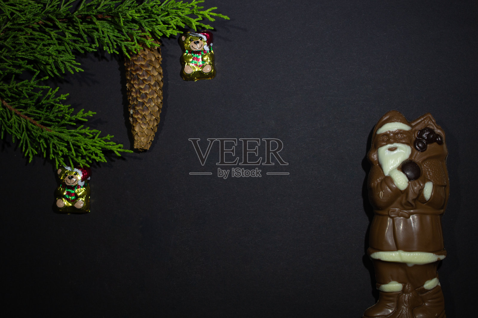 巧克力圣诞老人的照片由黑巧克力和白巧克力，冷杉果在黑色背景和绿色冷杉树枝和圣诞装饰熊照片摄影图片