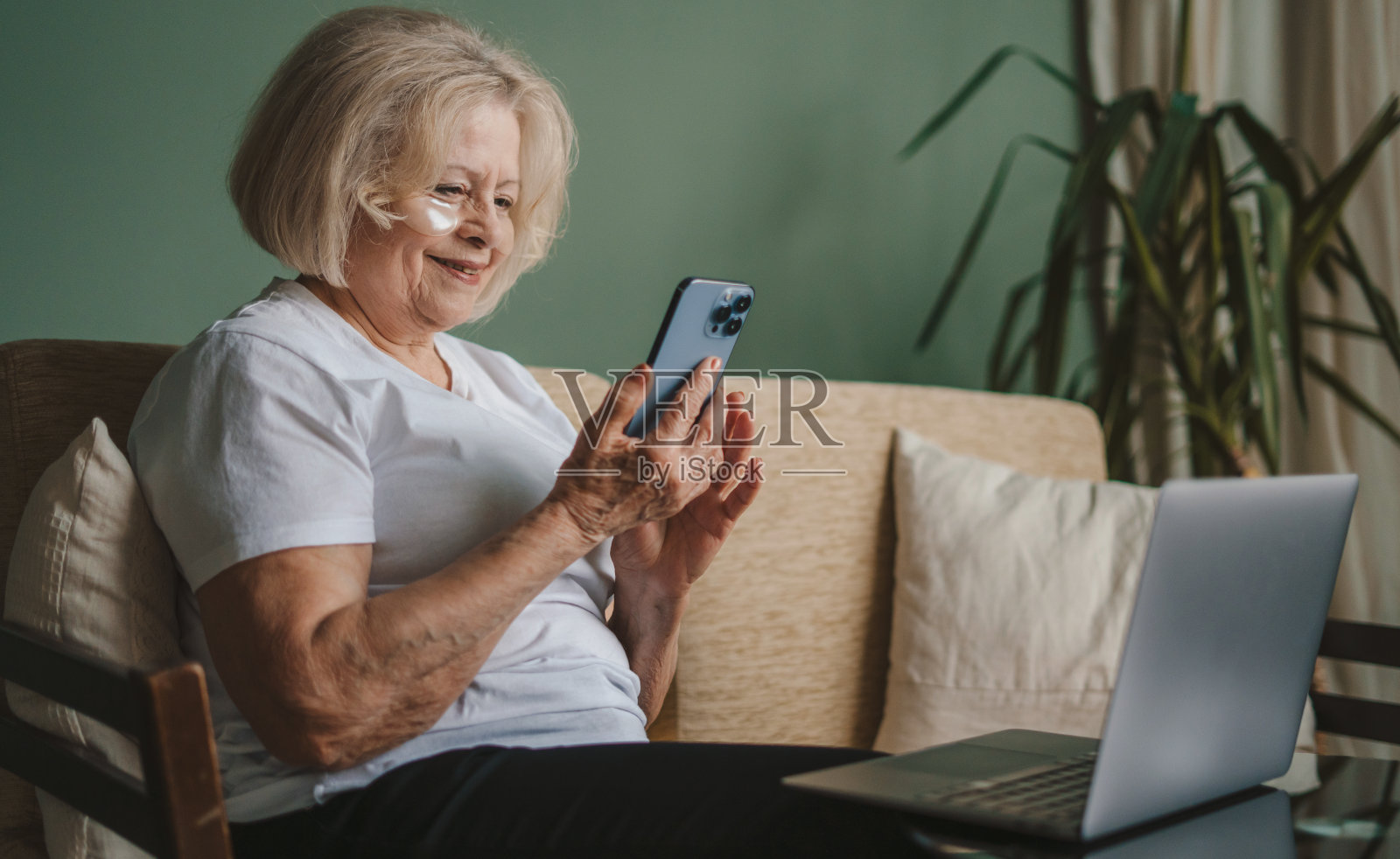 成熟女性，戴着眼罩，坐在沙发上，坐在笔记本电脑前，用着手机。手机通讯。照片摄影图片