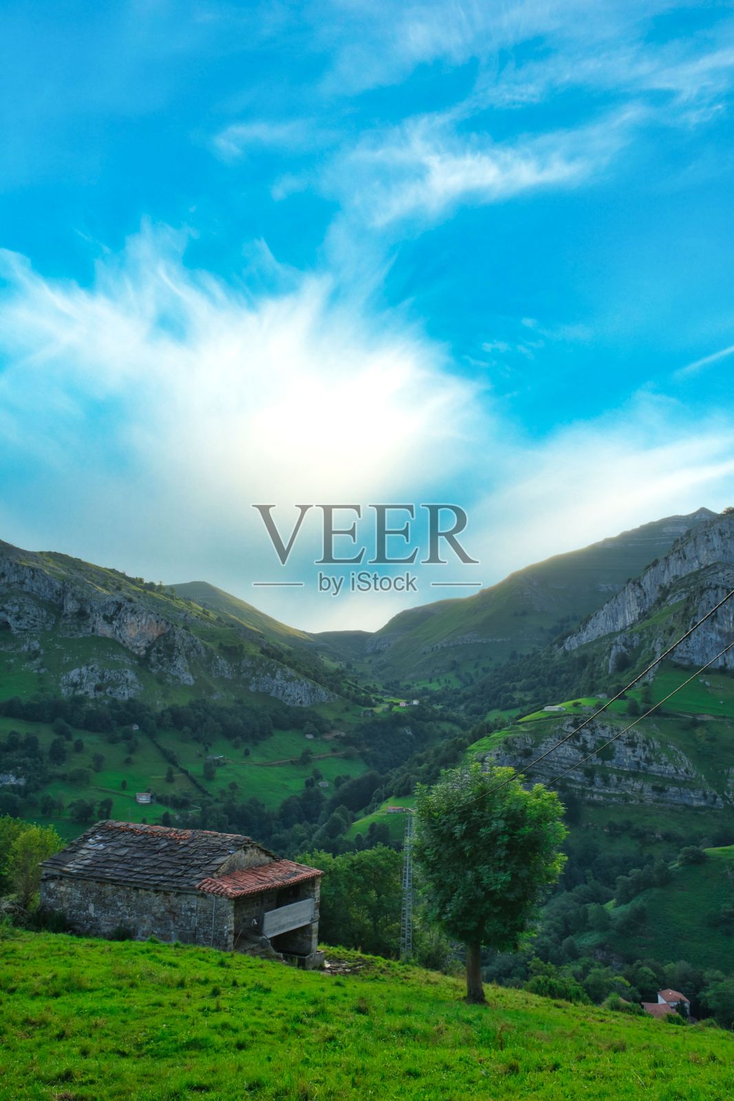 西班牙坎塔布里亚，蔚蓝多云的天空下，郁郁葱葱的乡村里的小石屋照片摄影图片