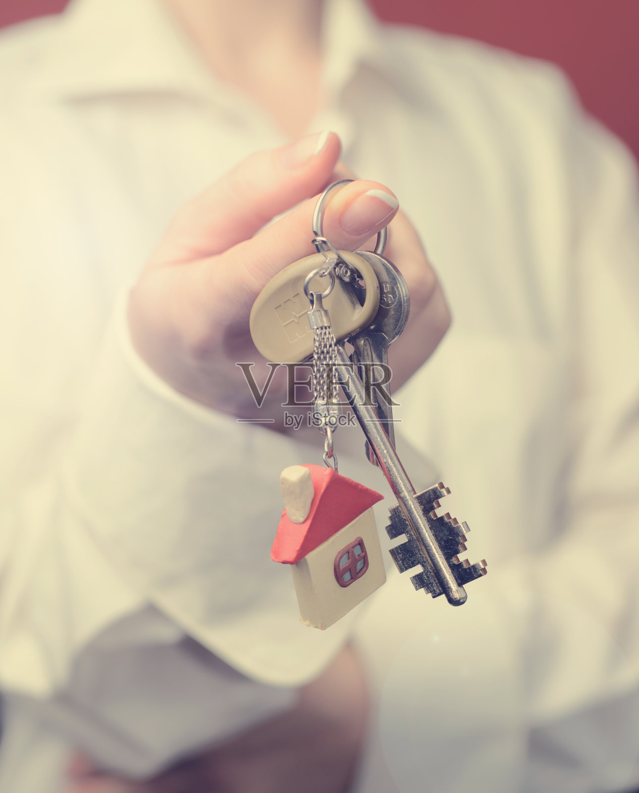 一位女士正在递钥匙。钥匙和房子形状的钥匙链。在橙色背景上照片摄影图片