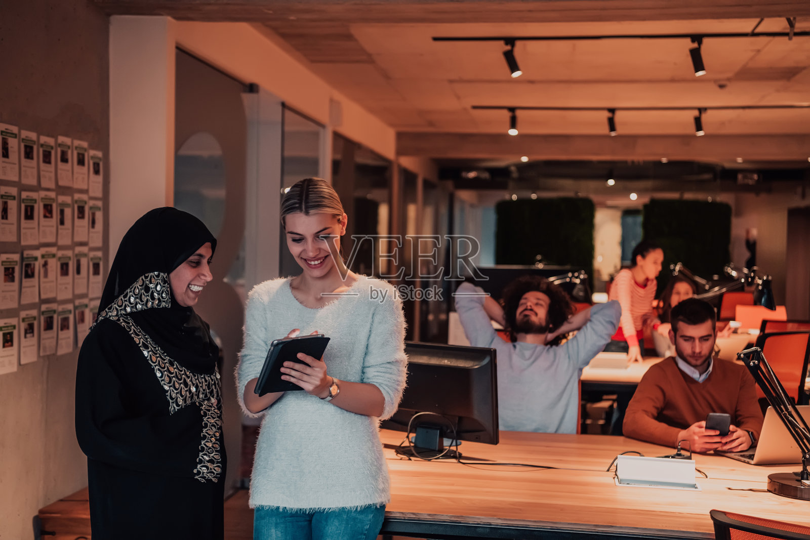 在现代办公室里一起使用平板电脑解决问题的穆斯林女商人和年轻女商人照片摄影图片