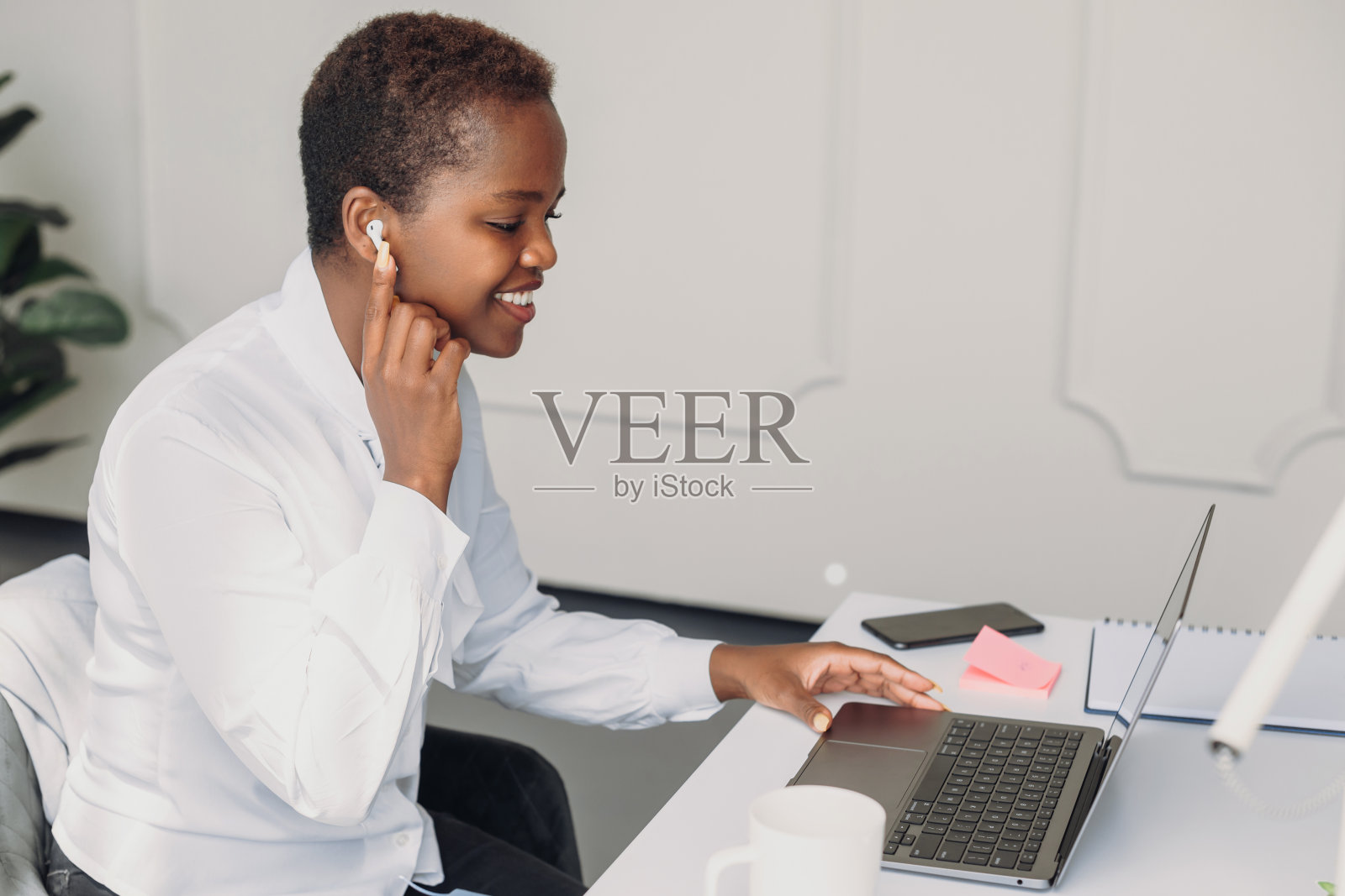 一个微笑的年轻非裔美国女商人坐在办公桌旁使用pc应用程序，在线交流观看网络研讨会的侧面视图。人，生活方式，现代科技和传播理念。通信网络。互联网技术照片摄影图片