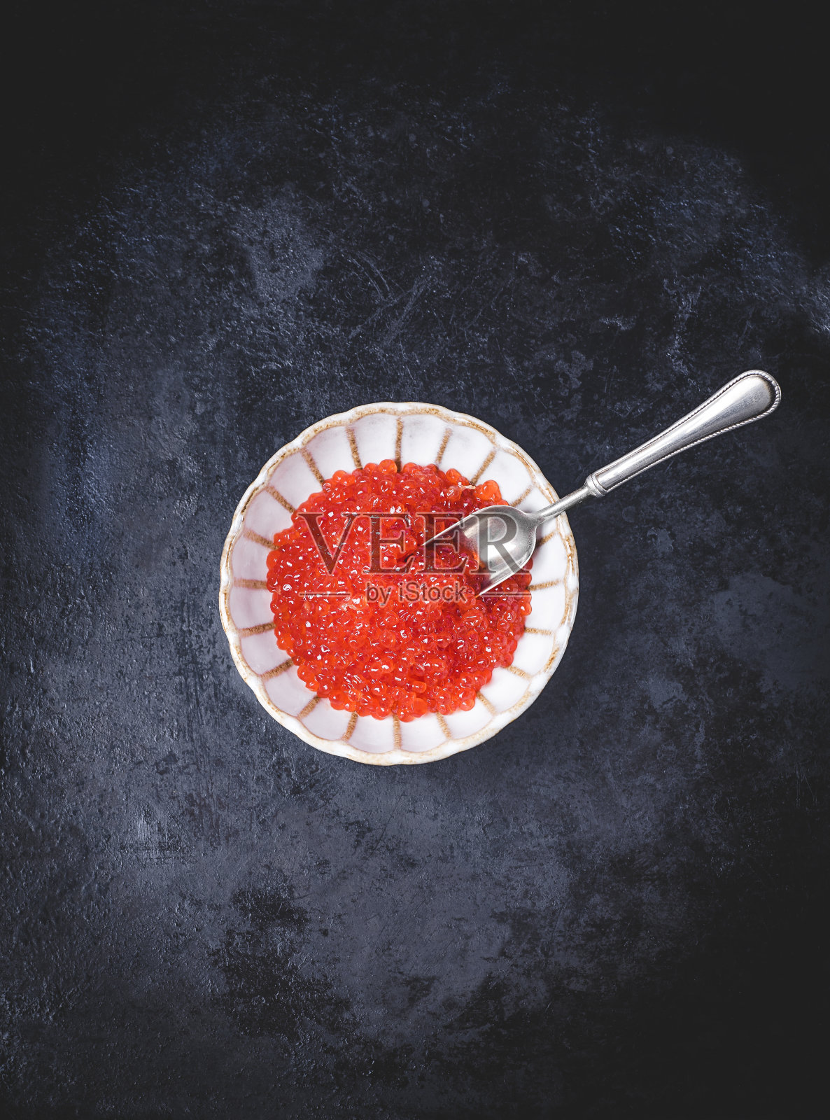 红色鱼子酱在一个美丽的陶瓷碗在一个花的形式与银匙在一个黑暗的金属背景，黑暗的关键。美学的最小构图。海鲜佳肴，日本料理的配料照片摄影图片