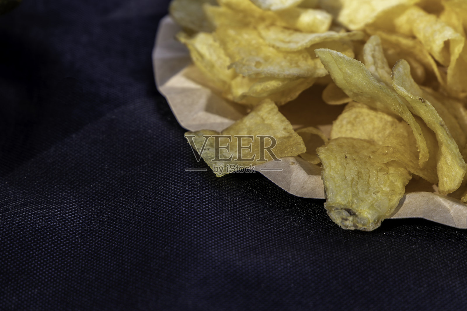 脆脆的薯片放在纸盘里，放在有质感的桌布上。快餐。有选择性的重点照片摄影图片