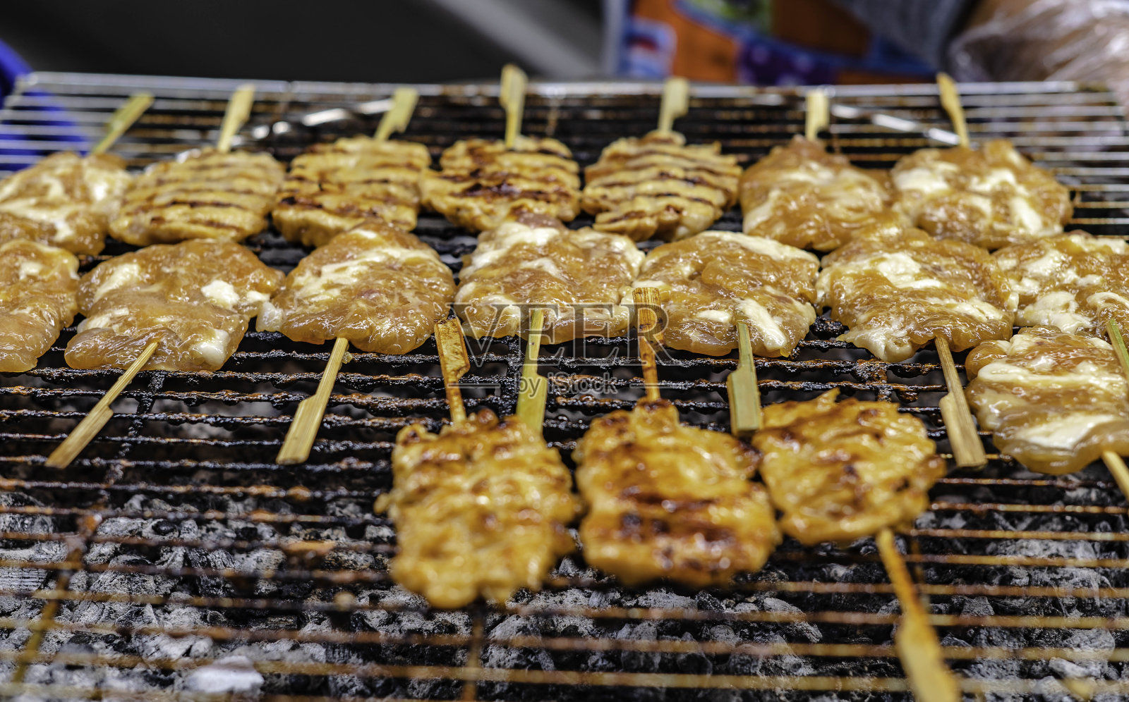在泰国曼谷的人行道上出售的牛奶腌猪肉串在竹架上的木炭上。照片摄影图片