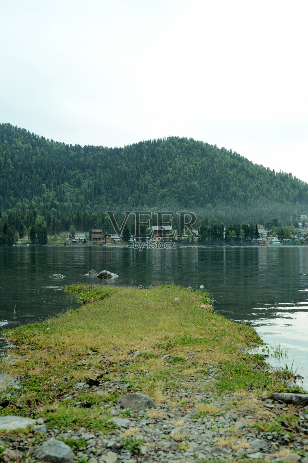 一片长满青草的狭长地带通往一个风景如画的湖泊的中心，周围环绕着高山。照片摄影图片