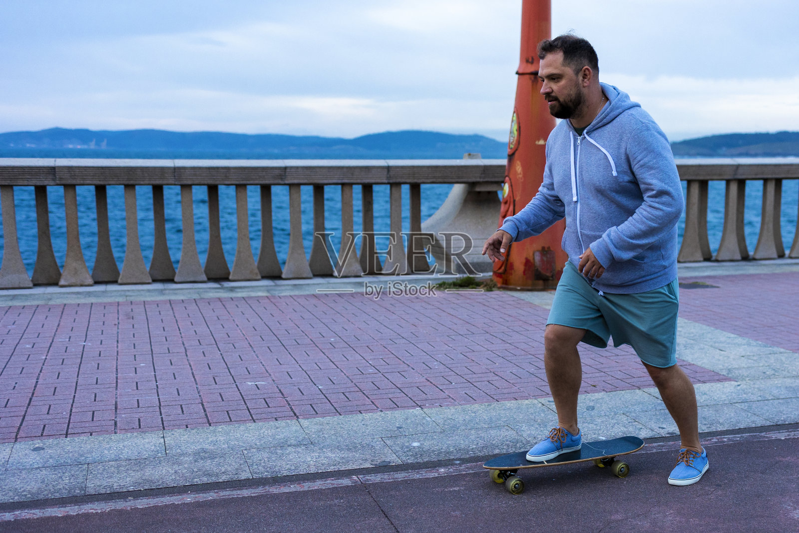 一个穿着绿色短裤和蓝色运动鞋的男人在玩滑板。照片摄影图片