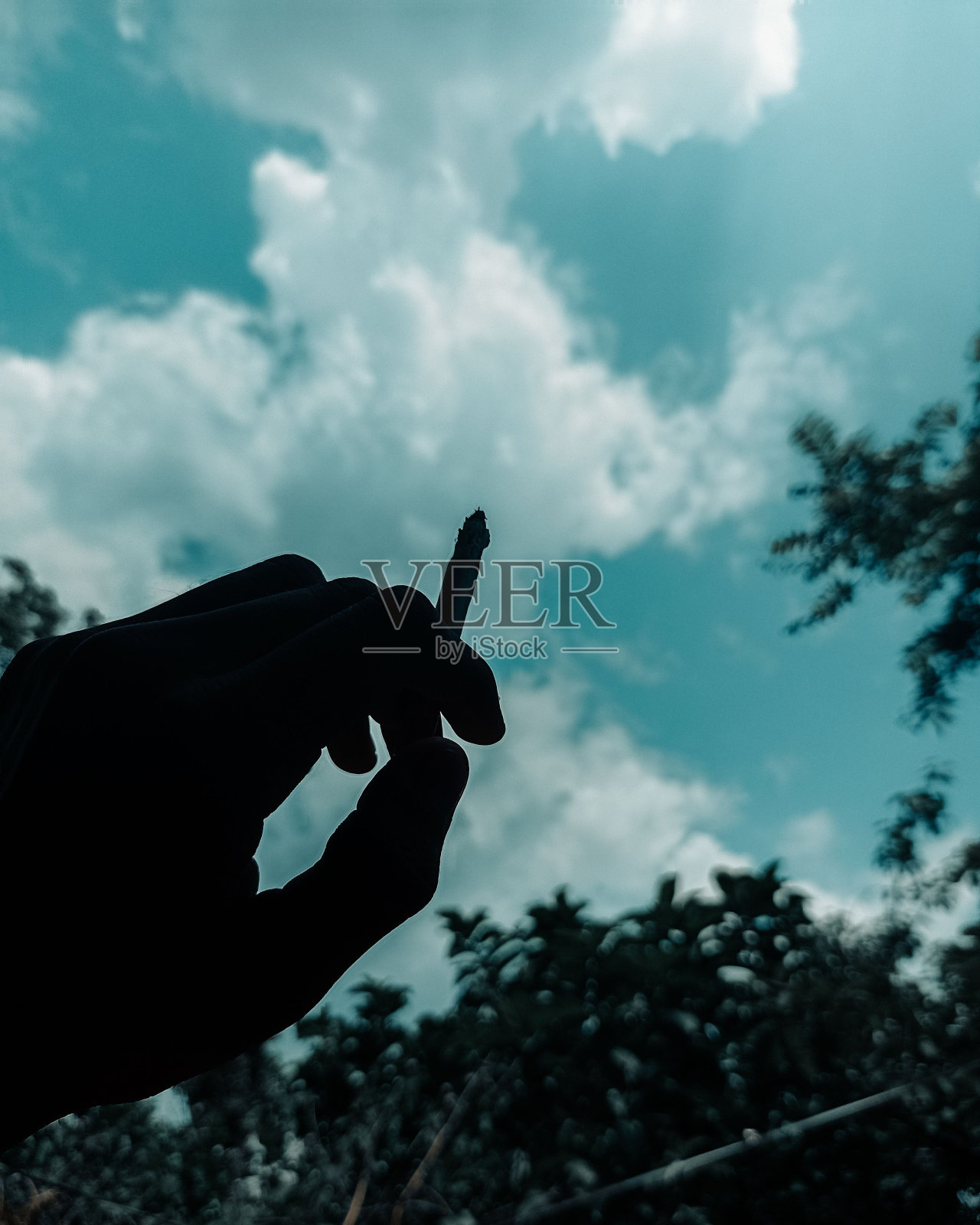 一个人的手拿着香烟的低角度镜头，背景是天空照片摄影图片