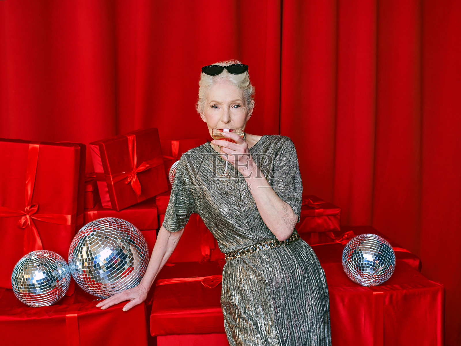 高级时尚优雅的女人与一杯气泡酒的红色背景。派对、时尚、庆典、反年龄概念照片摄影图片