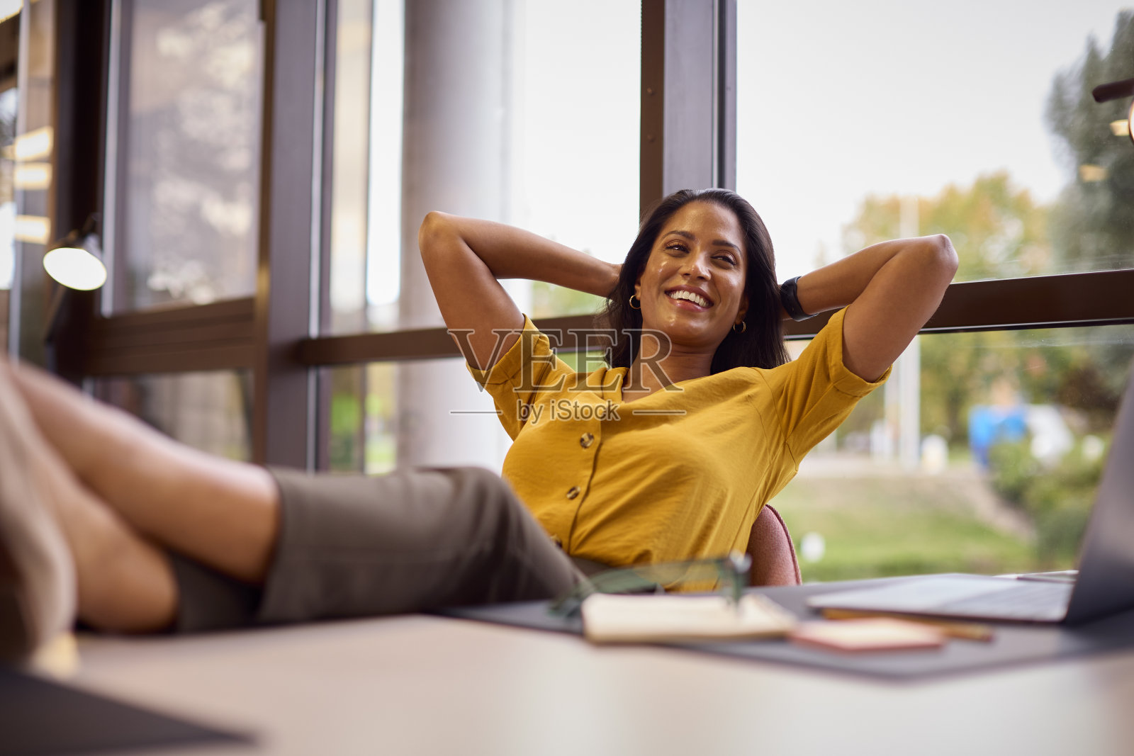 脚放在桌子上的成熟女商人在办公室休息照片摄影图片
