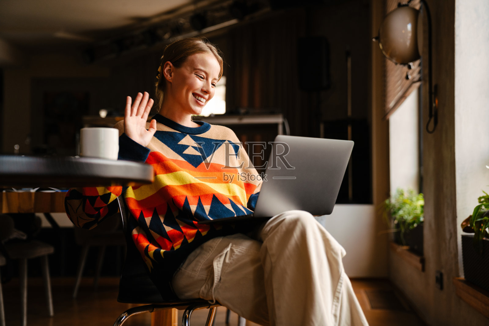 微笑的女人有视频电话通过笔记本电脑和挥手，而坐在咖啡馆照片摄影图片