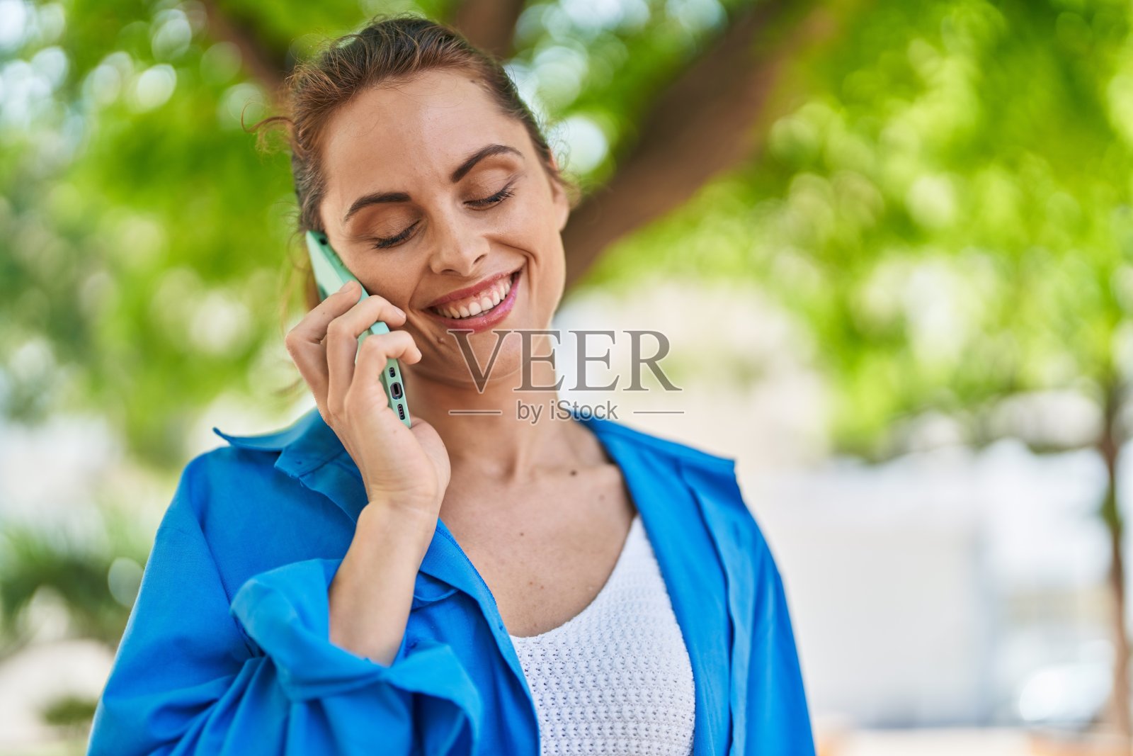 年轻女子微笑着自信地在公园用智能手机说话照片摄影图片