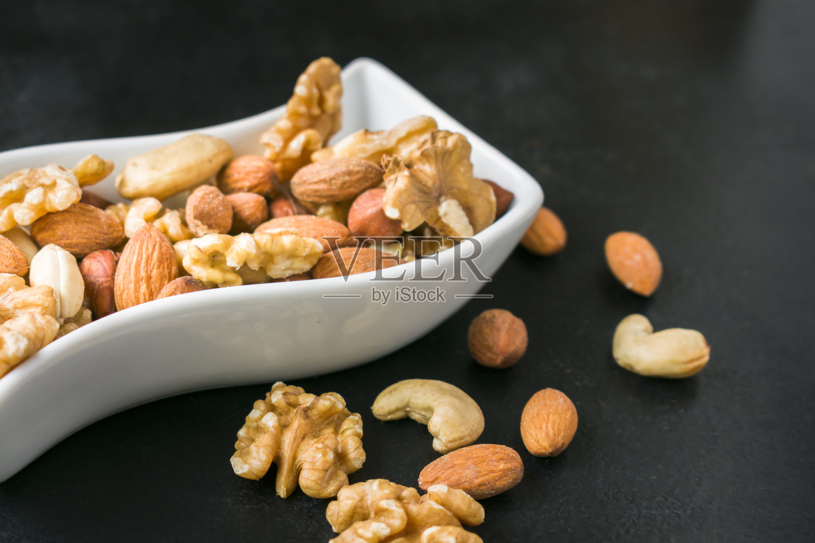 什锦坚果在白色形状碗在黑色背景。健康的素食饮食照片摄影图片