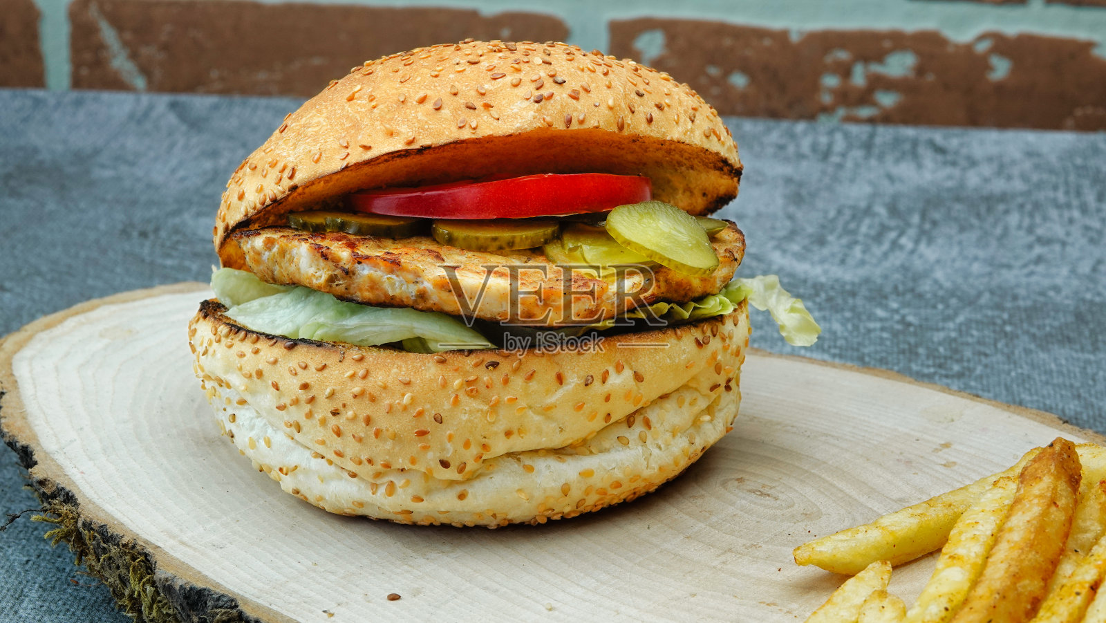 美味的鸡肉汉堡，炸薯条，生菜，西红柿和黄瓜泡菜在一个天然的木制托盘上的特写照片摄影图片