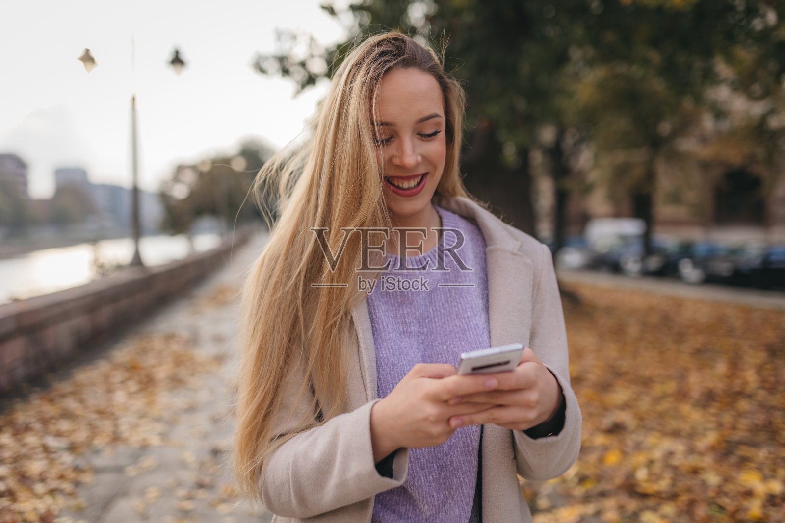 微笑的年轻女子在街上使用智能手机照片摄影图片