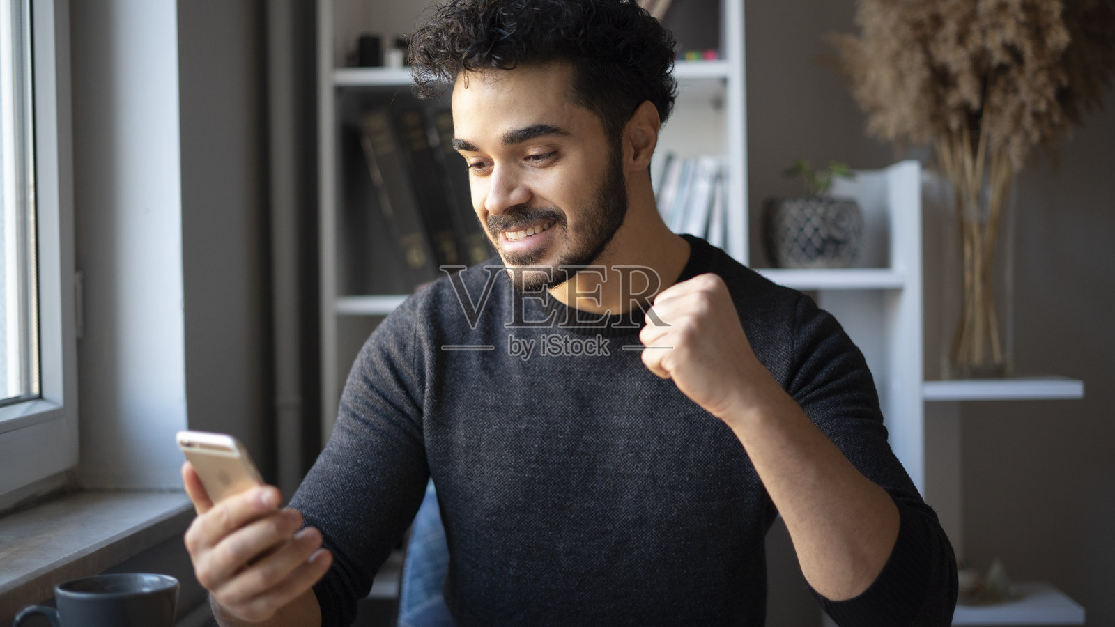 年轻人从手机上收到好消息，握紧拳头，高兴极了照片摄影图片