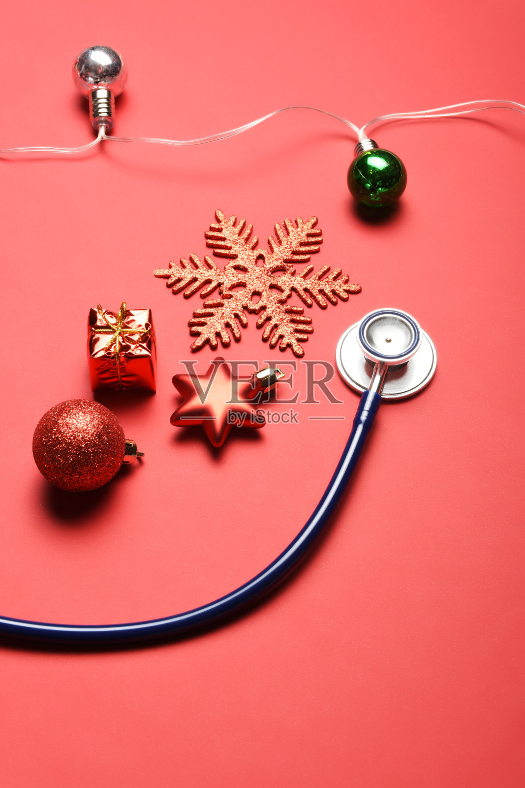 快乐健康的新年装饰。听诊器、圣诞彩灯和红色背景的圣诞装饰品照片摄影图片