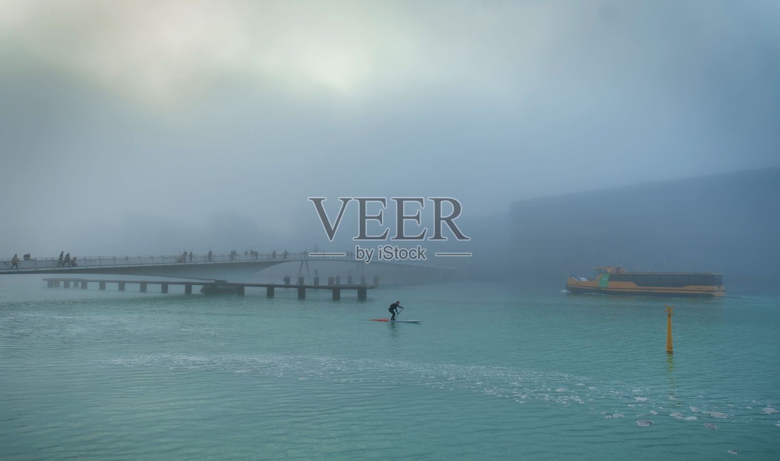 桥上笼罩着薄雾，一个人在冲浪板上，游船经过。照片摄影图片