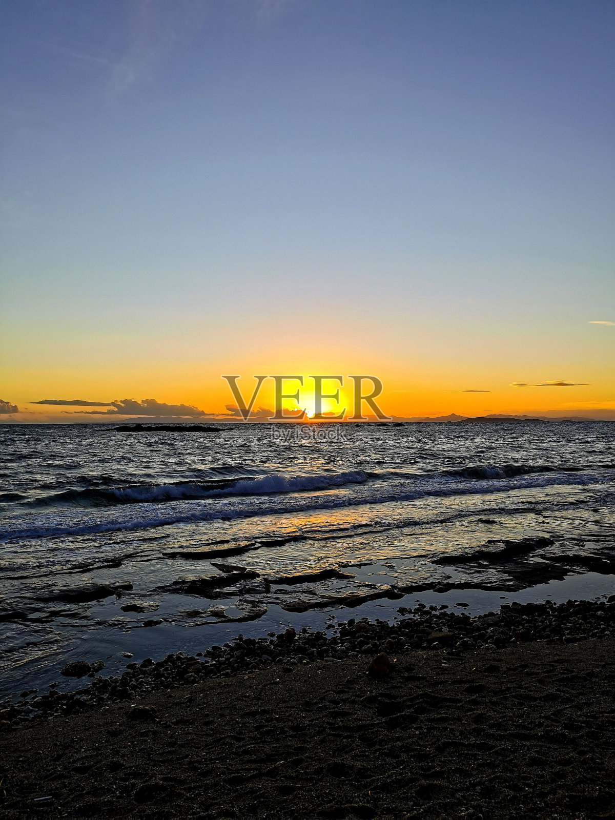 垂直拍摄的美丽日落在海滩上，海浪拍打着希腊的海岸照片摄影图片
