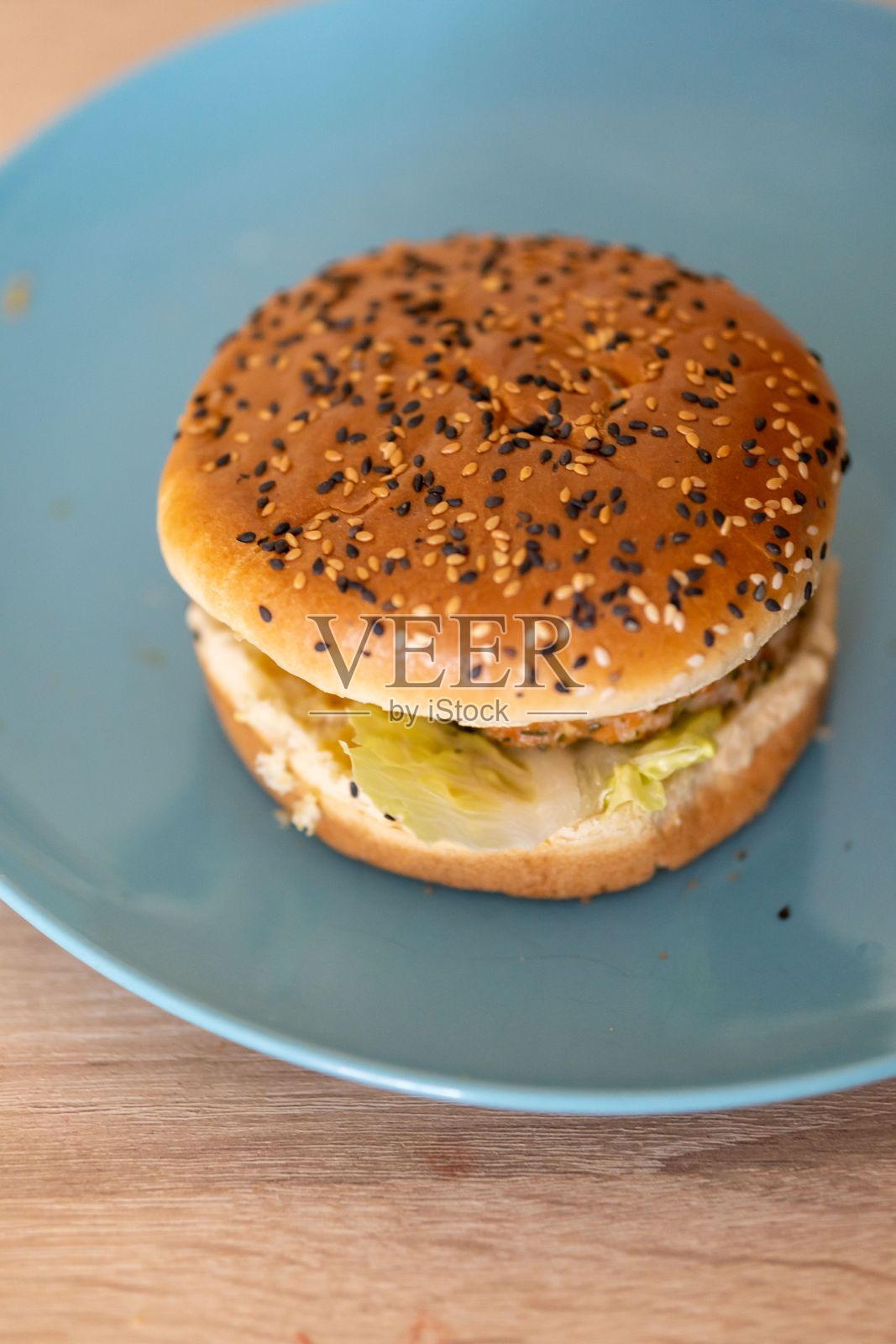 垂直拍摄的一个小汉堡在一个蓝色的圆形盘子在桌子上照片摄影图片
