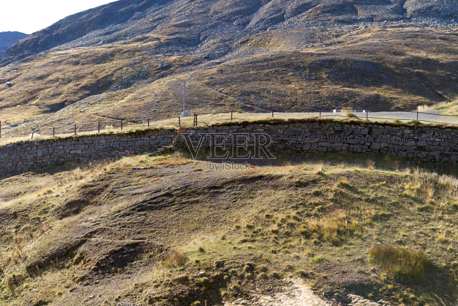 在一个阳光明媚的夏末的一天，瑞士山口Furkapass与清晨的阳光和诗人约翰·沃尔夫冈·歌德在石墙上的文字。照片摄影图片