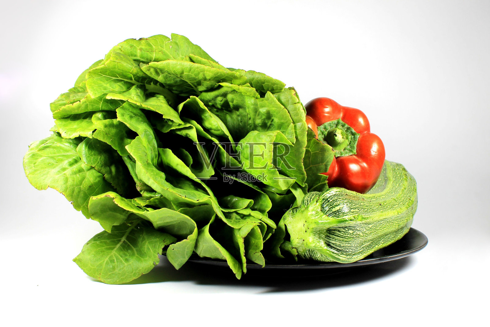 一个白色背景上有蔬菜的黑色盘子的特写。照片摄影图片