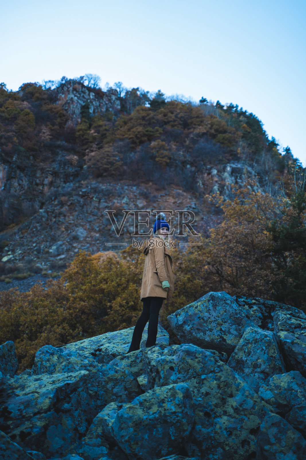 美丽的女人走在秋天的森林里，爬上了山顶。照片摄影图片