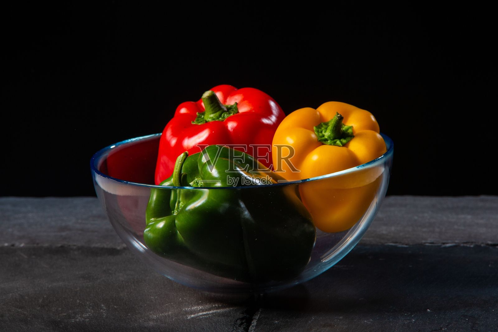 特写三个彩色辣椒在一个碗在一个黑暗的背景照片摄影图片