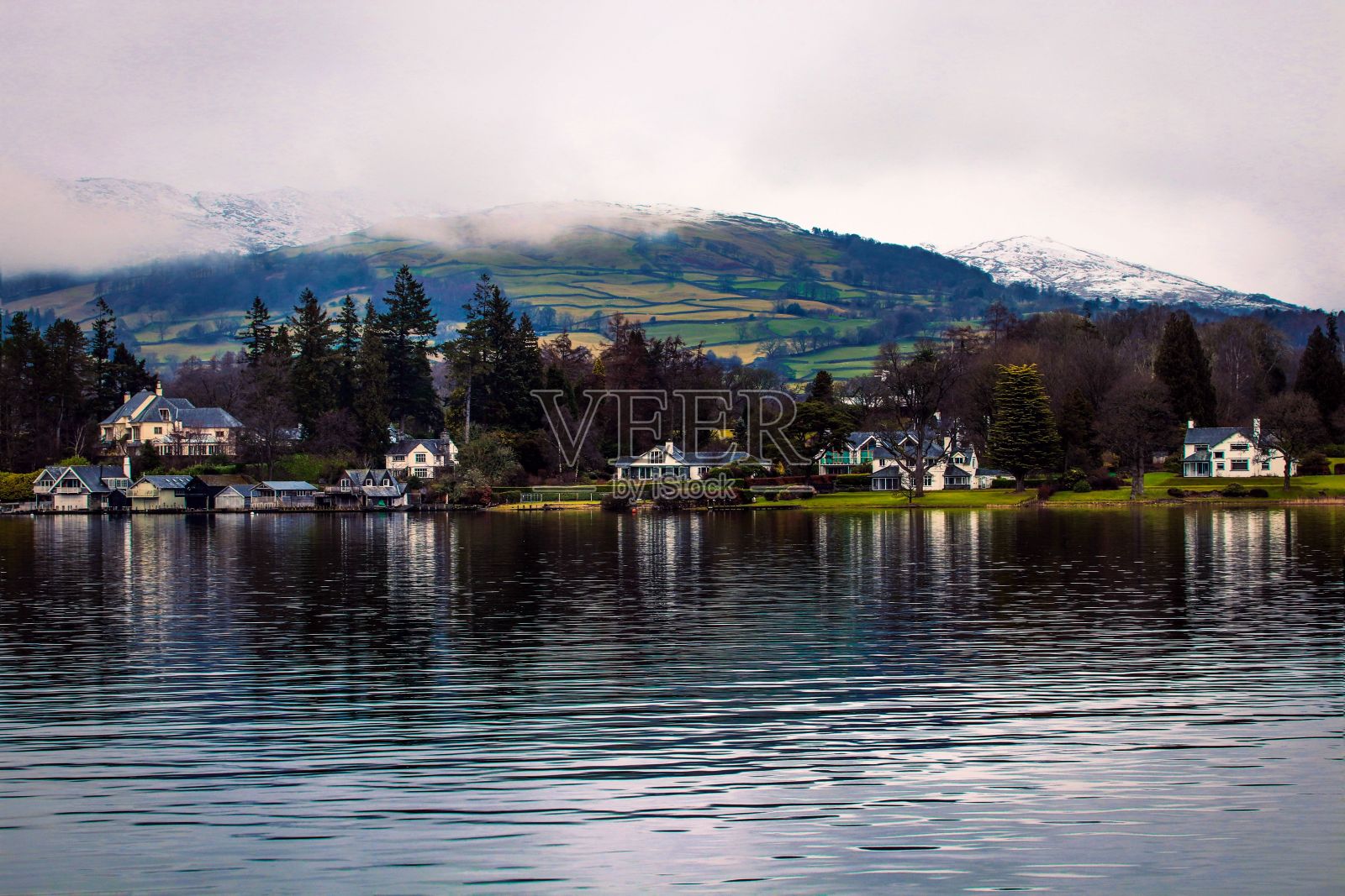 宁静的湖泊周围环绕着常绿的森林和云下的山丘照片摄影图片