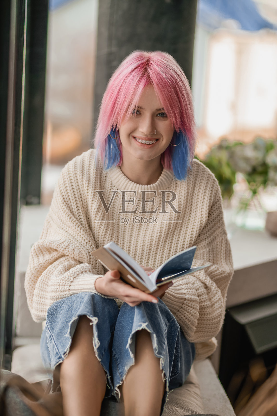 一个粉红色头发的女孩在窗边看书照片摄影图片