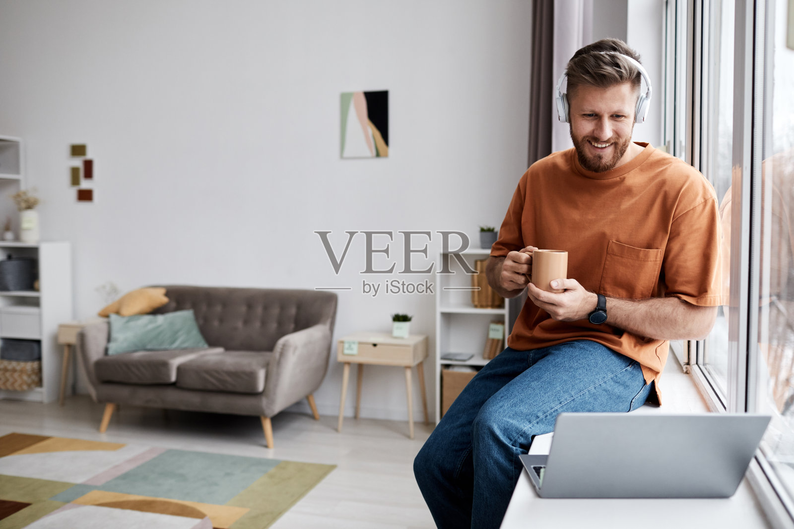 快乐的年轻人，一杯咖啡坐在窗前的笔记本电脑前照片摄影图片