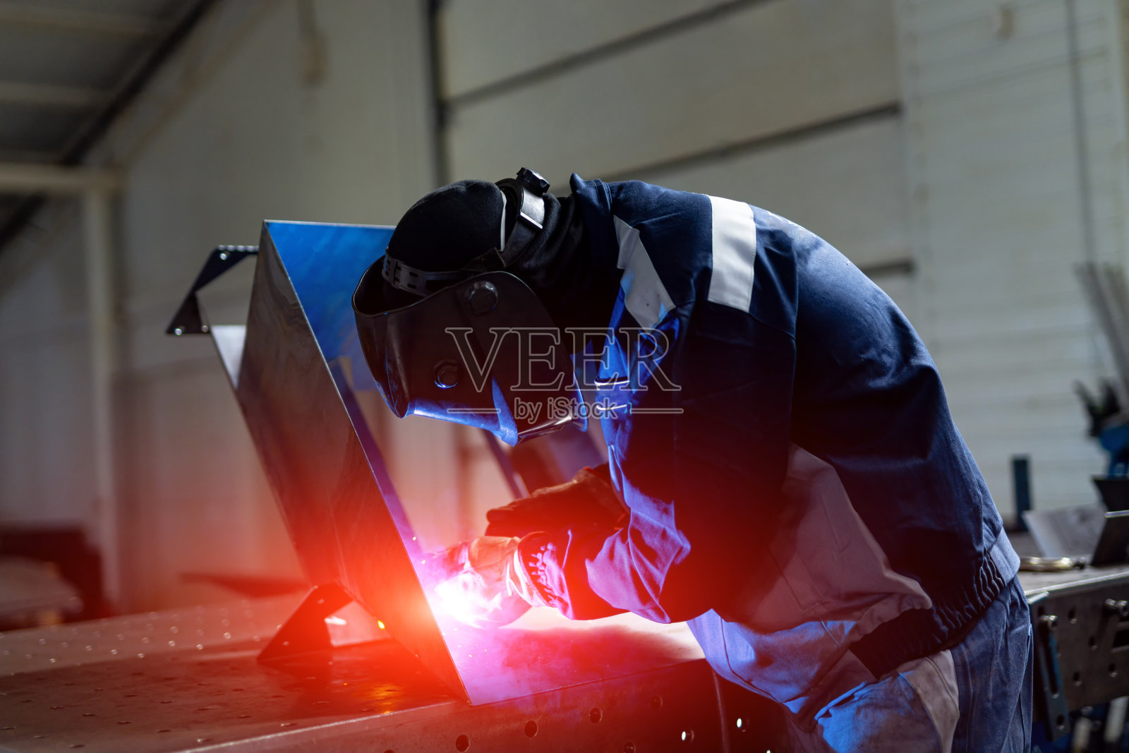 英俊的工人制服与金属制品。戴着防护帽焊接金属的人。照片摄影图片