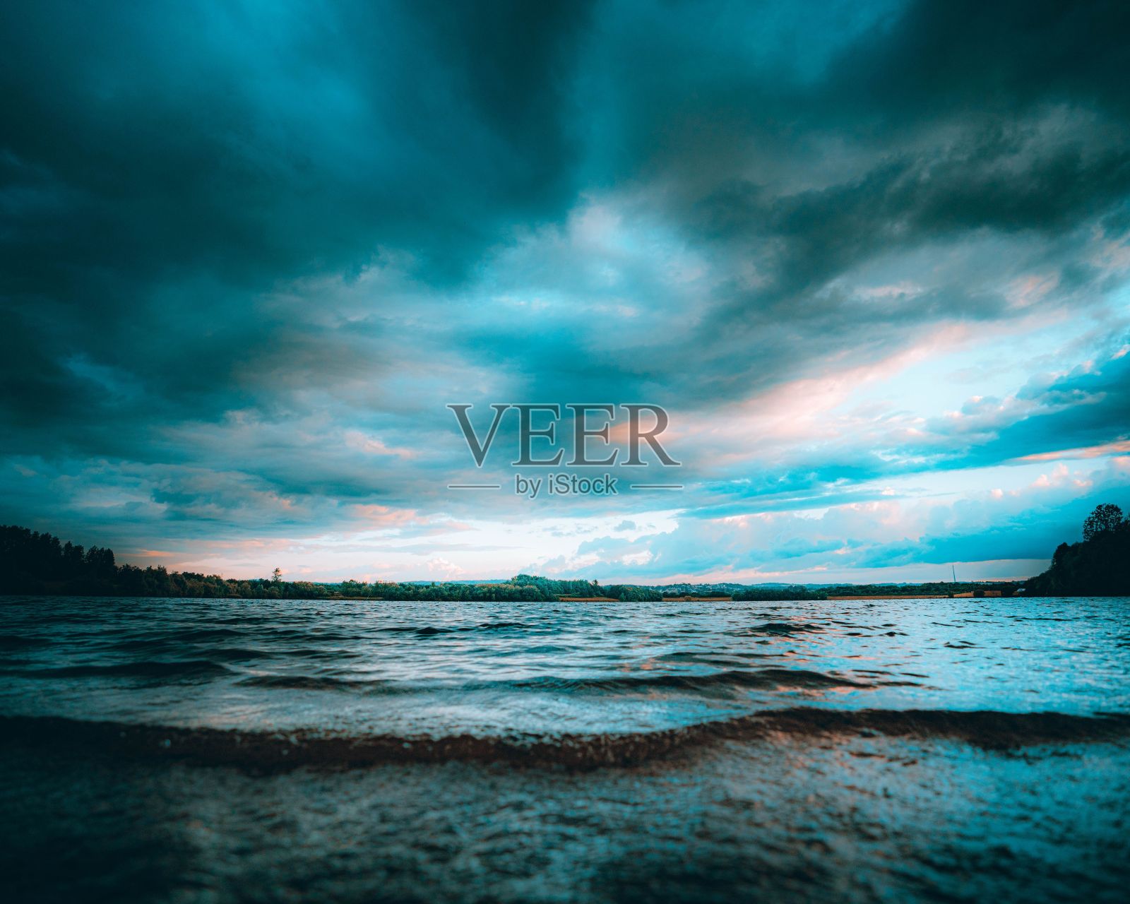 在阴沉的一天，多云的天空下，以波浪和树木为背景的湖泊的戏剧性景色照片摄影图片