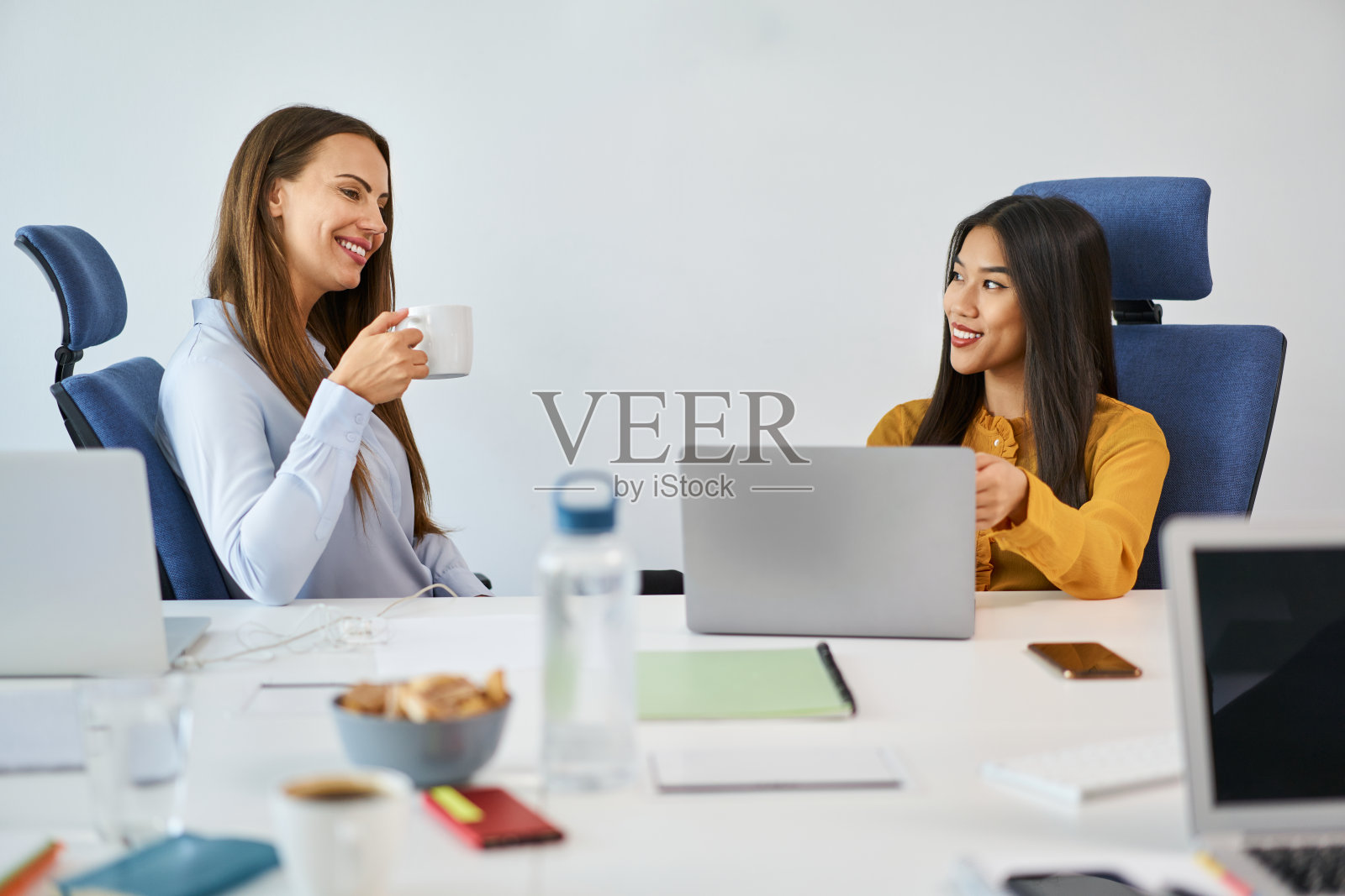 微笑的女人在办公室交谈。两个女同事在办公室开会时商量生意照片摄影图片