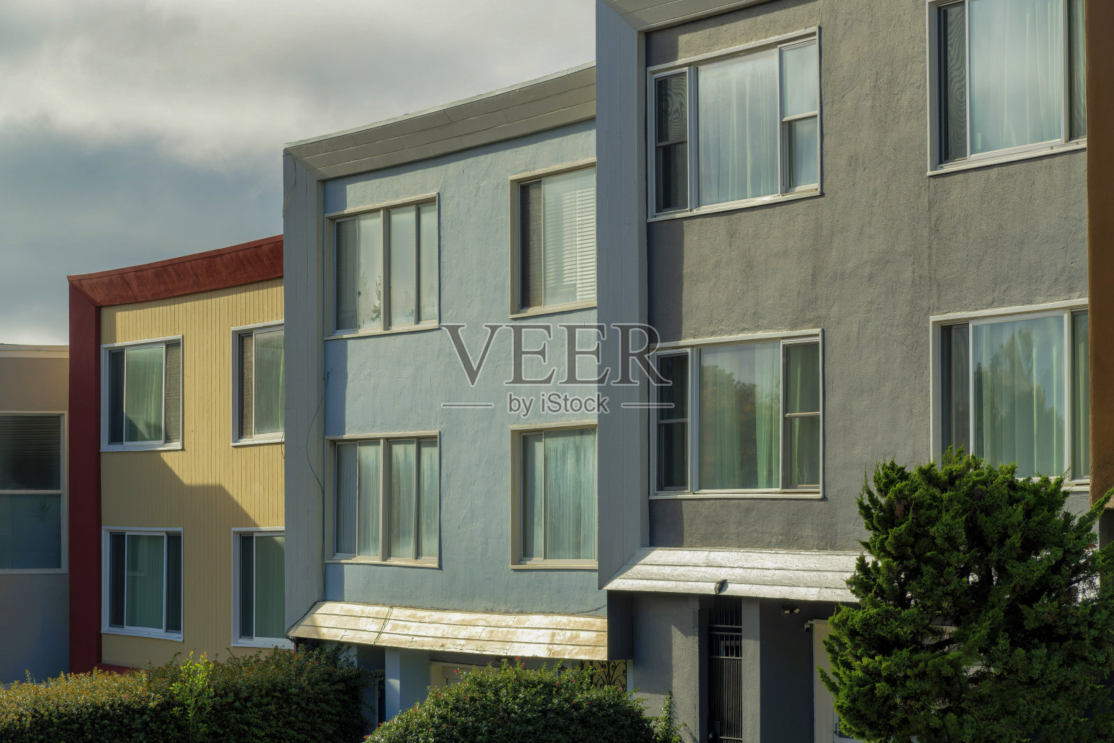 在傍晚的阳光下，在社区或郊区的多云和灰色的天空背景下，一排方形的彩色房屋照片摄影图片