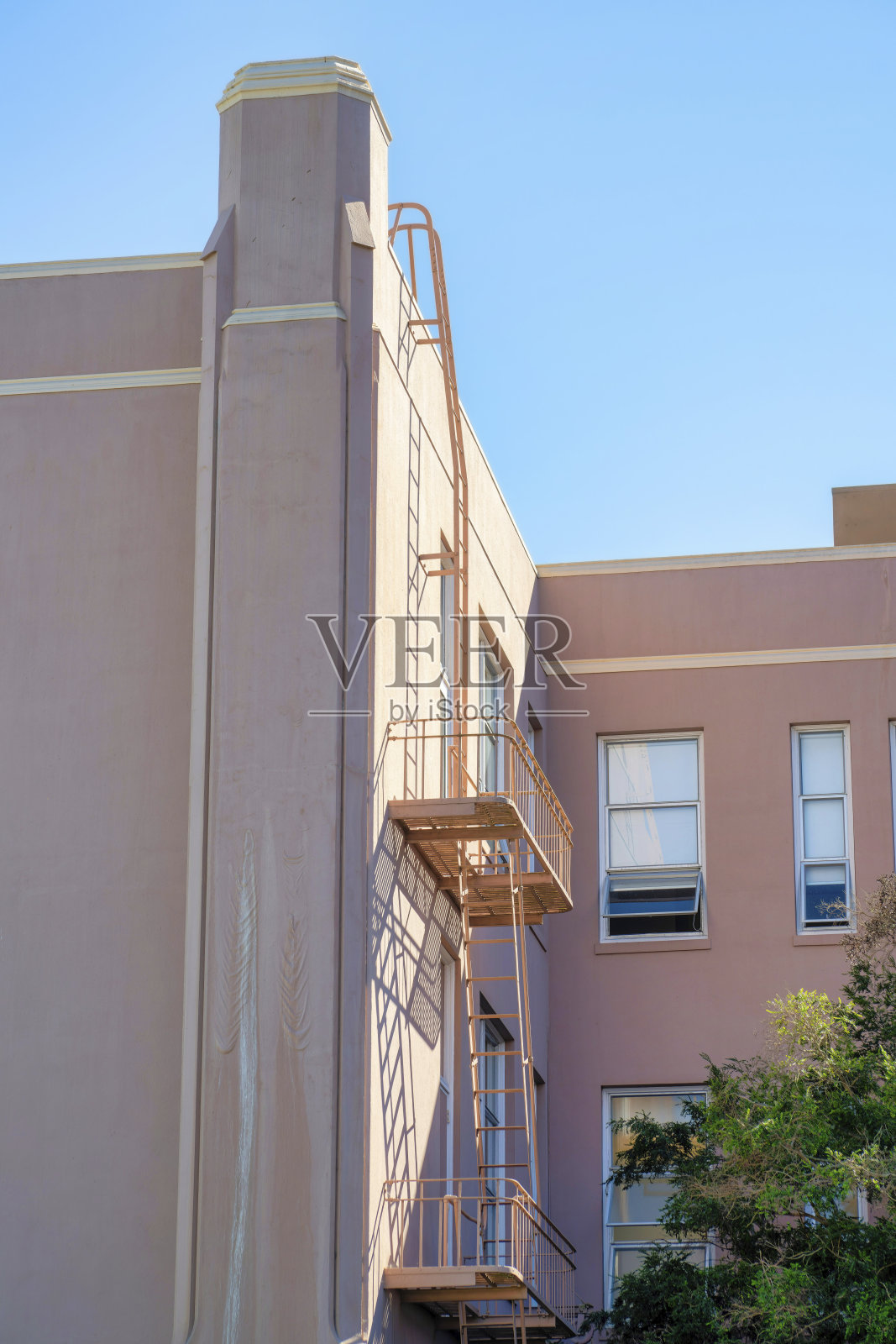 粉红色或橙色灰泥建筑，在阳光下有消防梯或逃生阳台，在蓝天背景下有一些阴影照片摄影图片