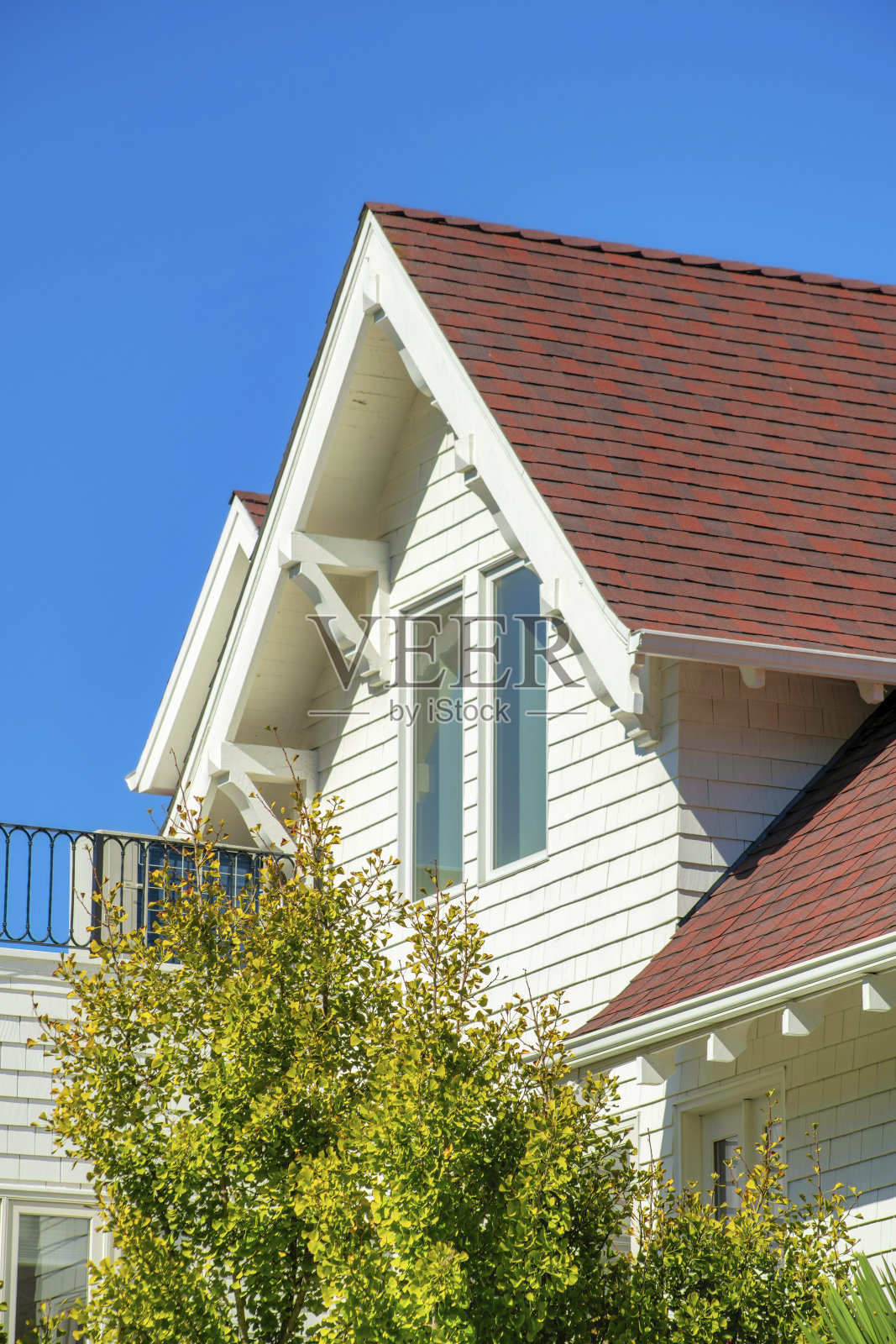 白色木板条房屋，带有面板和红棕色山墙风格的屋顶，前院树木和清晰的蓝天背景照片摄影图片